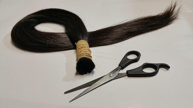 Een donkere rechte haarbundel met een elastiek naast een schaar op een lichte achtergrond.