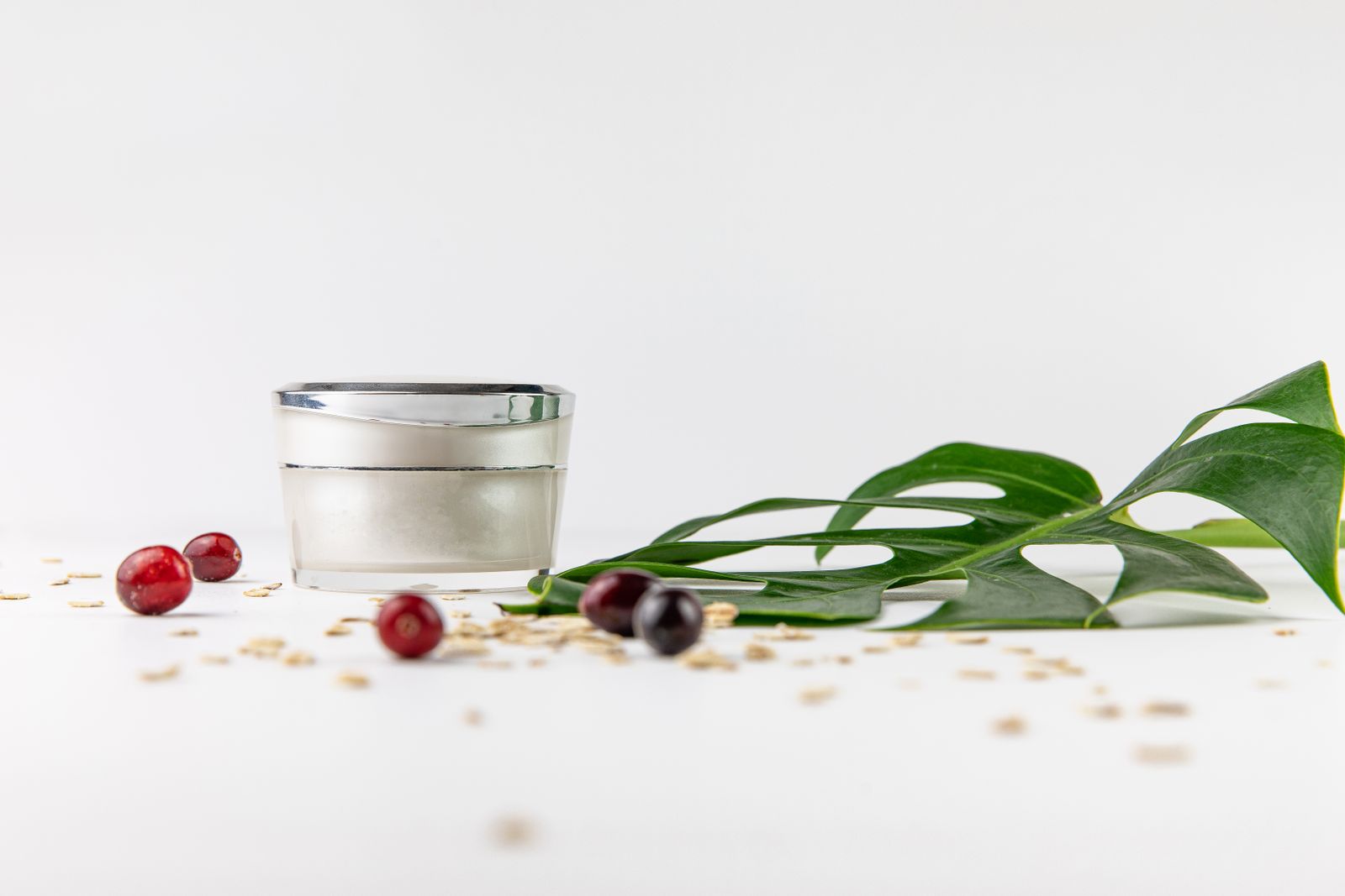 Ongelabelde pot witte cosmetische crème op een lichte ondergrond met groen blad.